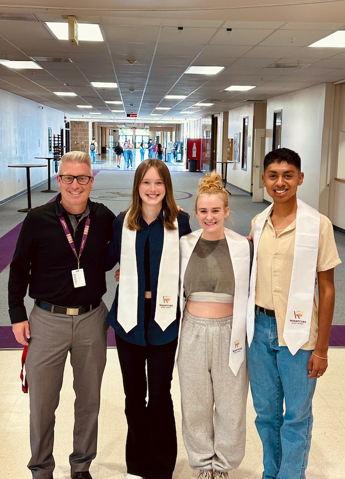 Group of high school students standing together in a school hallway with an adult male